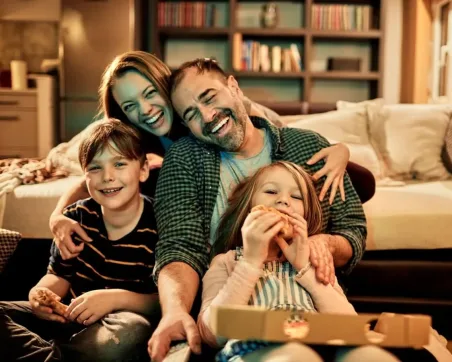 Gezin zit samen op de bank te lachen en pizza te eten terwijl ze televisie kijken via IPTVPrime, een IPTV abonnement – ideaal voor wie een goedkope IPTV oplossing zoekt of IPTV wil kopen voor thuisentertainment.